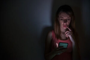 A girl sitting in darkness and looking at her phone in sadness and tension Image