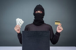 A robber standing with some cash and bank card in with hand and face covered Image